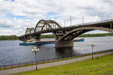 A tug pushing a heavy barge on the spring river under a bridge