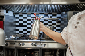 Professional chef holding a foam siphon in a restaurant kitchen