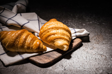 fresh baked croissants on towel and wooden cutting board on concrete grey surface in dark