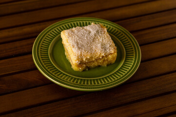 Pineapple iced cake with desiccated coconut on a green plate on wooden table
