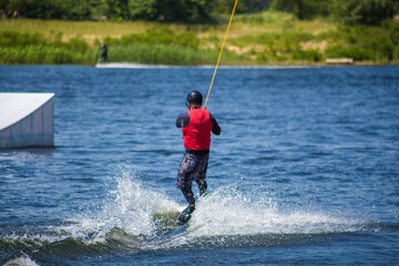 The man does wakeboarding on the water in the summer in a helmet and wetsuit.