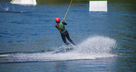 The man does wakeboarding on the water in the summer in a helmet and wetsuit.