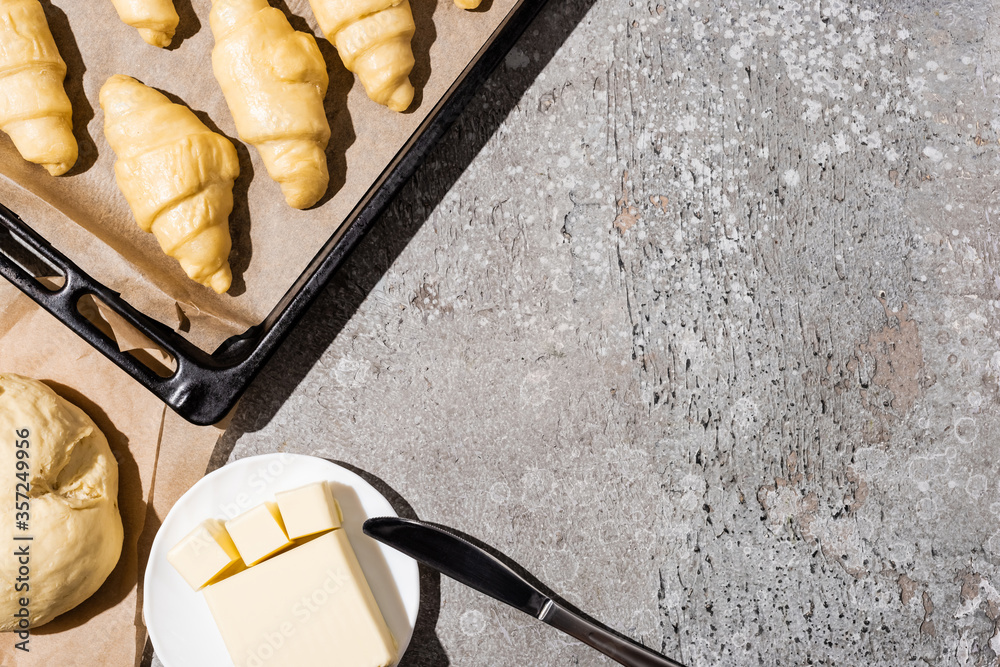 Wall mural top view of uncooked croissants on baking tray near dough and butter on concrete grey surface