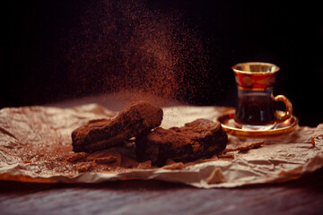 Delicious homemade chocolate brownies and cup of coffee composition on dark background. Chocolate bars are sprinkled with cocoa powder. Dessert aesthetics