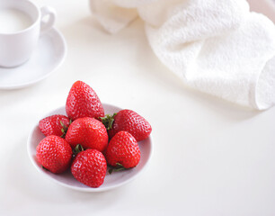 Fresh strawberries lie on a saucer, next to a mug of milk and a towel