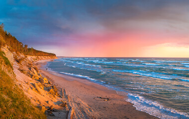 Baltic sea in colorful sunset colors with storm clouds in background. Turquoise water with waves, and sandy coastline.