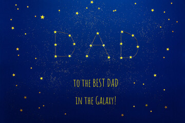 Applique of the constellation word Dad from star confetti on blue cardboard. Signature to the best in the galaxy. Greeting card Happy Father's day. Selective focus. Top view, mock up.