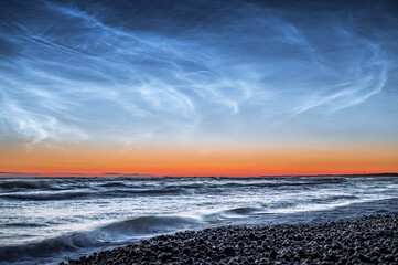Baltic sea at night time with Noctilucent clouds. Waves in motion with clear night sky. 
