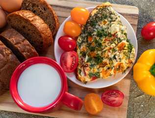 omelette with tomato, herbs, bread and peppers on wooden board for breakfast