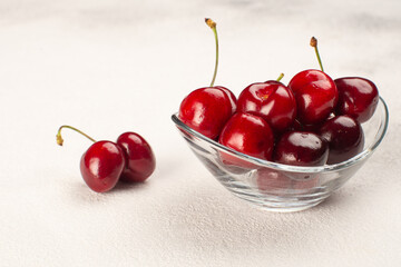 Fresh ripe cherries in glass bowl on light concrete table.Close up of raw berries.