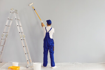 Worker painter paints a wall.Back view. Professional builder makes repairs. - obrazy, fototapety, plakaty