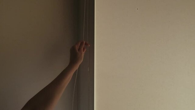 hand opens blackout roller jalousie. Window in the Interior with roller blinds. louvres on the window.