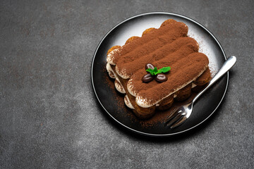 Classic tiramisu dessert on ceramic plate on dark concrete background