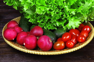 Fresh vegetables on a wooden background. A grenn salad, radishes, and tomatoes on a table. Rustic style. Vegetarian food. Raw, organic vegetables. Healthy food.
