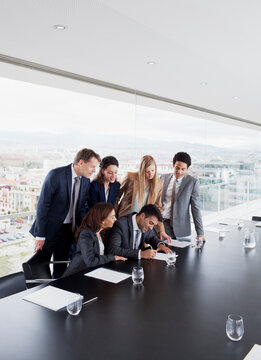 Business People Watching Businessman Sign Contract In Conference Room