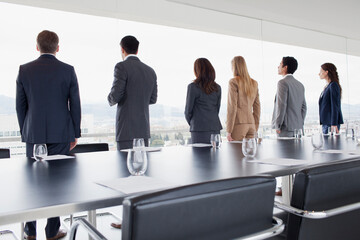 Business people in a row looking out conference room window
