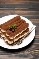 Classic tiramisu dessert on ceramic plate on wooden background