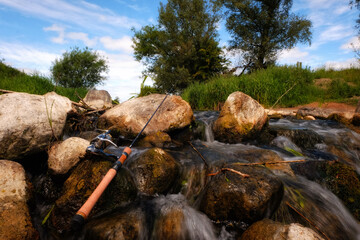 Waterfall on trout fishing stream with fishing rod and reel