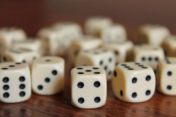 White dice, lie on a dark brown table. Random order. Back and side plan blurred.