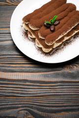 Classic tiramisu dessert on ceramic plate on wooden background