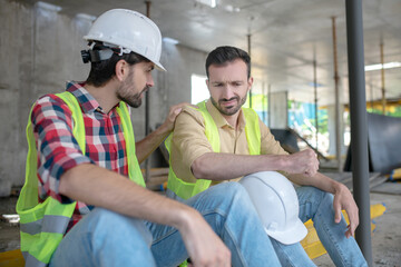 Building worker putting his hand on shoulder of his demotimated coworker, trying to support him