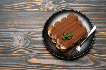 Classic tiramisu dessert on ceramic plate on wooden background