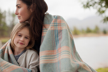 Portrait smiling daughter wrapped in blanket with mother at lakeside