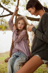 Mother braiding daughter‚Äôs hair on swing at lakeside