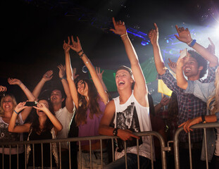 Enthusiastic crowd with arms raised behind railing at concert
