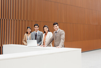 Portrait of confident business people with laptop at ledge in office