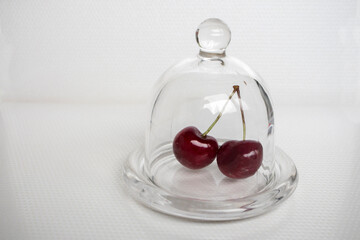 Two red cherries isolated under a glass lid on a white background.