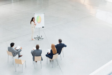 Fototapeta premium Businesswoman at flipchart leading meeting in lobby