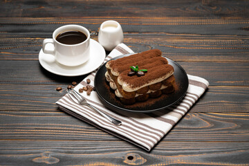 Classic tiramisu dessert on ceramic plate, milk or cream and cup of coffee on wooden background