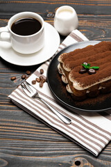 Classic tiramisu dessert on ceramic plate, milk or cream and cup of coffee on wooden background