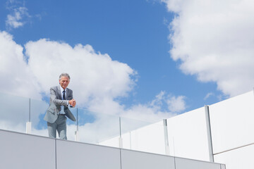 Portrait of confident businessman with hands clasped on balcony