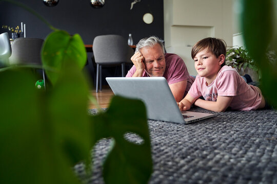 Father and son lying on floor, working on laptop
