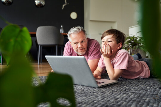 Father and son lying on floor, working on laptop