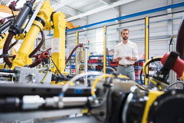 Male robotics expert standing by computer-aided manufacturing technology at factory