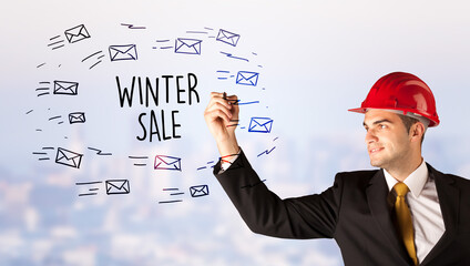 Handsome businessman with helmet drawing WINTER SALE inscription, contruction sale concept