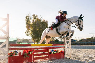 Teenage girl riding white horse while training for obstacle course on ranch
