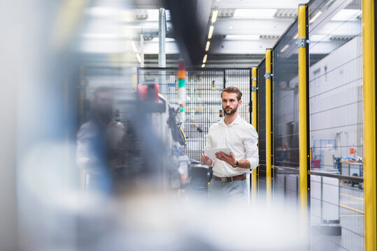 Young male engineer standing with digital tablet while looking away at manufacturing industry