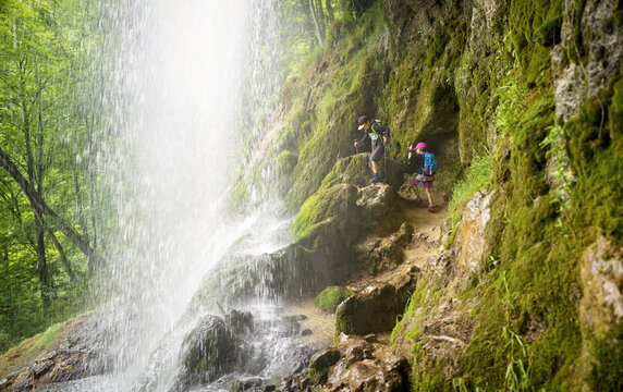 Boy and girl hiking on rock formation under Urach Waterfall in forest