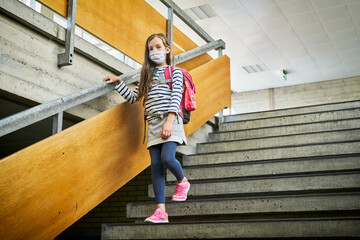 Girl wearing mask in school walking down stairs