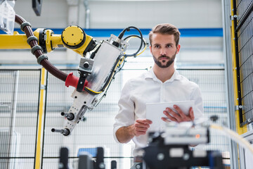 Young robotics engineer looking away while standing by machinery in factory