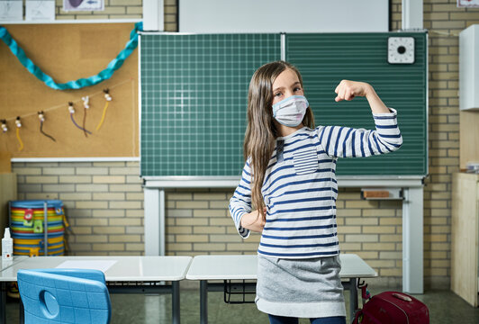 Portrait of girl wearing mask in classroom flexing muscles