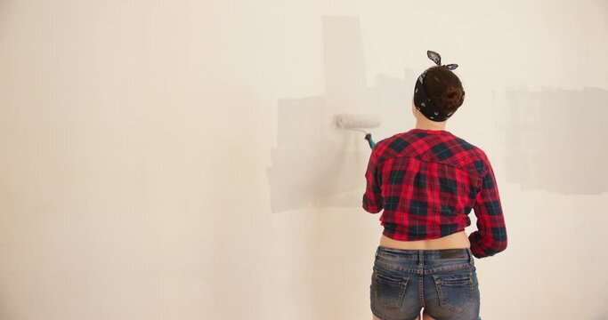 Pretty woman painting walls with roller. DIY Home decoration and renovation.