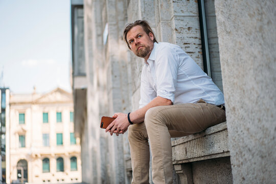 Businessman sitting in niche of a building holding smartphone