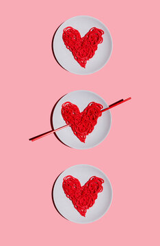 Studio shot of three plates with?red-colored?heart-shaped?spaghetti against pink background