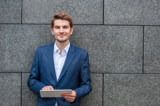 Portrait of young businessman with tablet standing at a wall