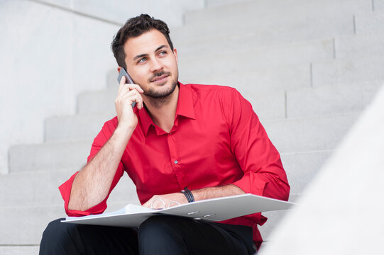 Smiling businessman calling with folder sitting on the stairs